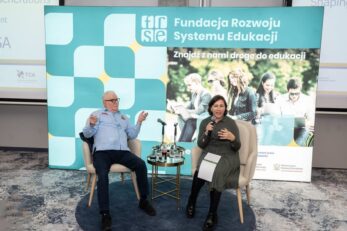 Two panelists seated on stage with a small table and microphones; backdrop displays 'Fundacja Rozwoju Systemu Edukacji' and students.